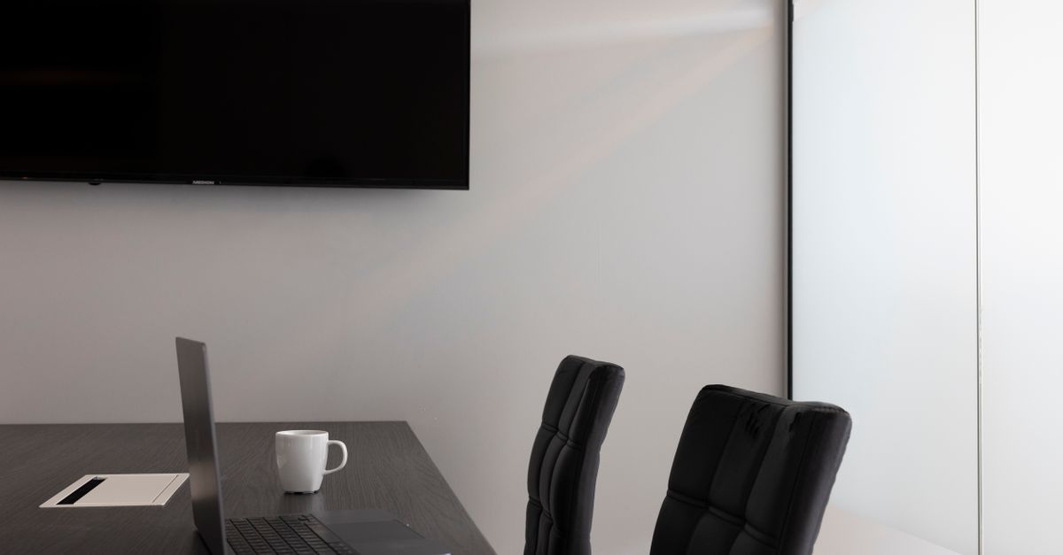 A sleek, modern office setup with a laptop, cup, and TV in an empty conference room.