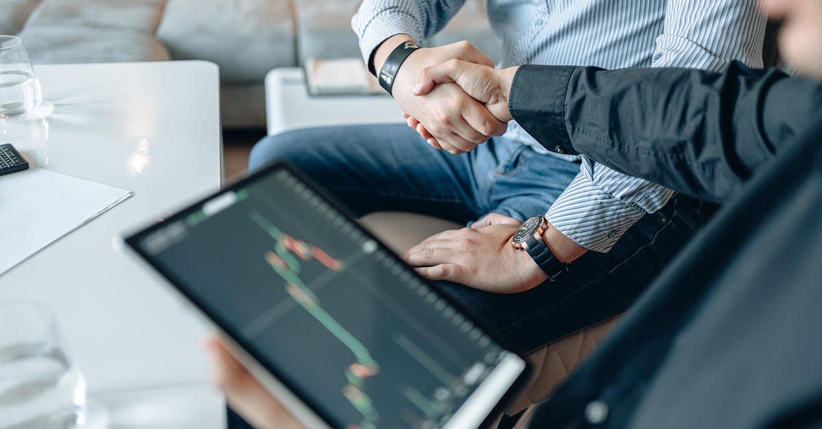 Two businesspeople shaking hands over stock market data on a tablet.
