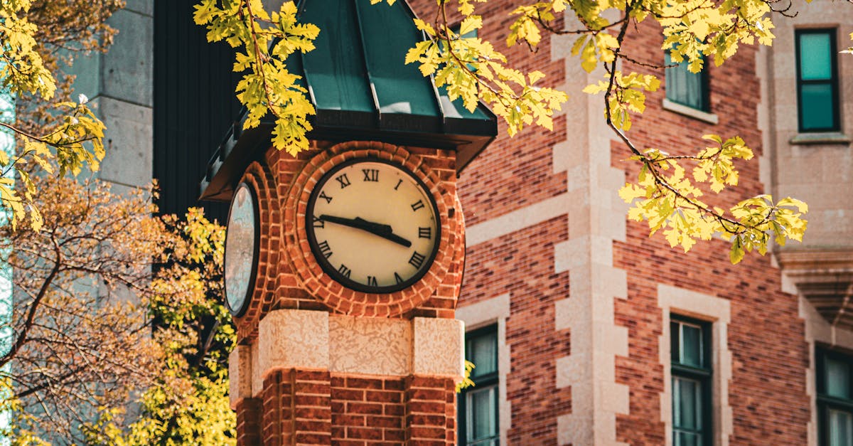 Charming clock tower framed by vibrant autumn leaves against a classic brick building.