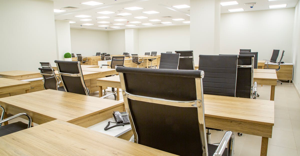 Spacious modern office with wooden desks and leather chairs in a bright, well-lit room.