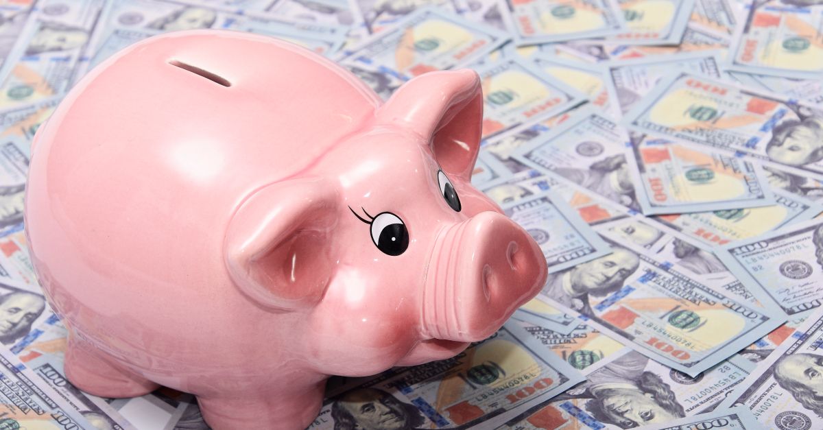 Pink ceramic piggy bank placed on a spread of US dollar bills symbolizing savings and financial security.