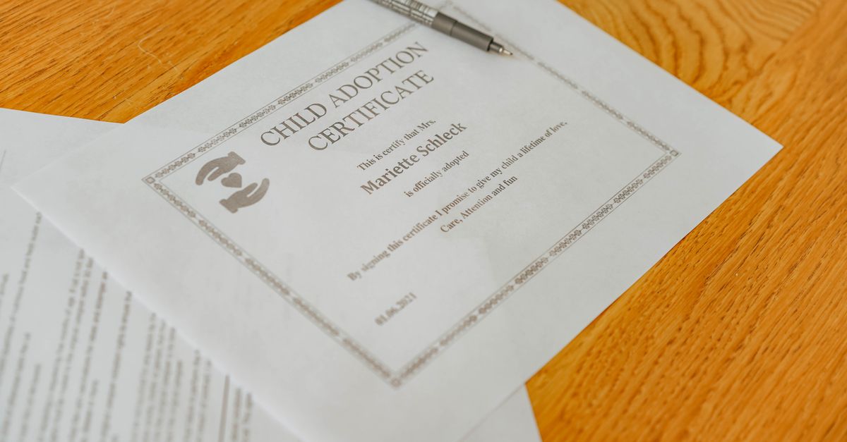 Close-up of a child adoption certificate and documents with a pen on a wooden table.