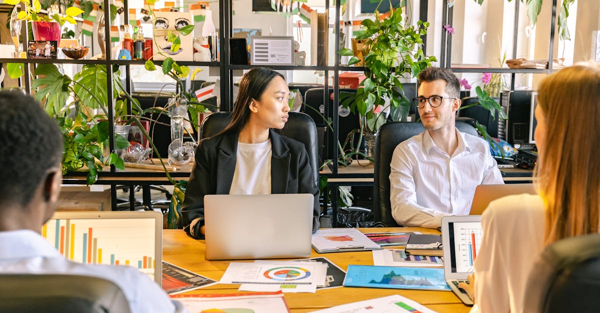 A diverse team of professionals discussing projects in a plant-filled office setting.