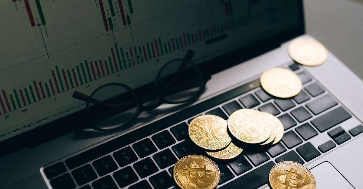 Golden Bitcoins on a laptop keyboard with a stock market chart on the screen, symbolizing cryptocurrency trading.
