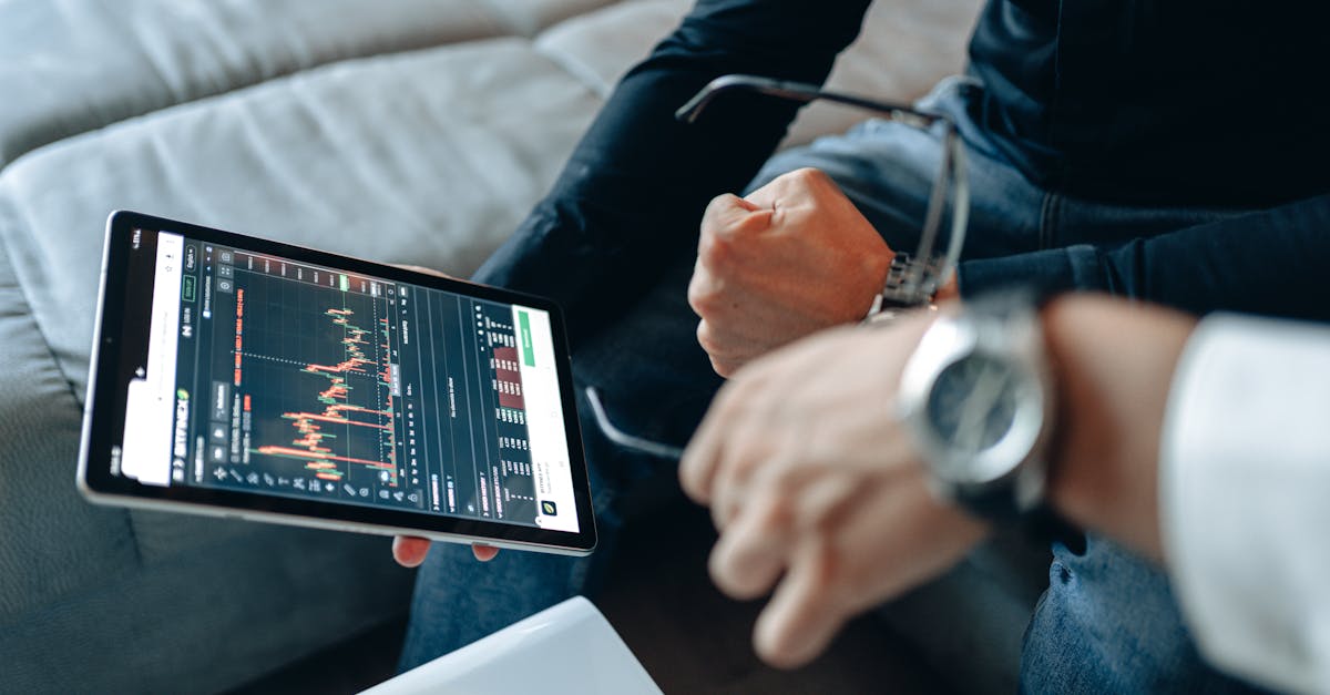 Close-up of tablet with trading charts, held by people analyzing online trades indoors.