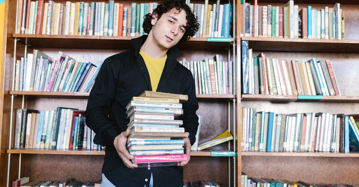 A young adult male holding a stack of books in a library, symbolizing education and learning.