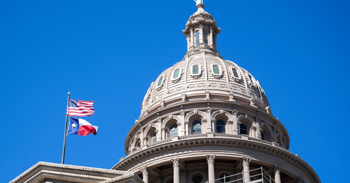 Close-up view of the Texas State Capitol dome in Austin with flags against a clear blue sky.