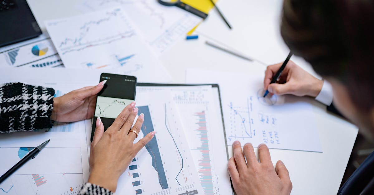 Overhead view of people analyzing financial graphs and data with smartphone and documents.