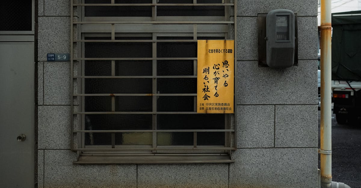 A Japanese urban building facade featuring a window with traditional signage and metal grating.