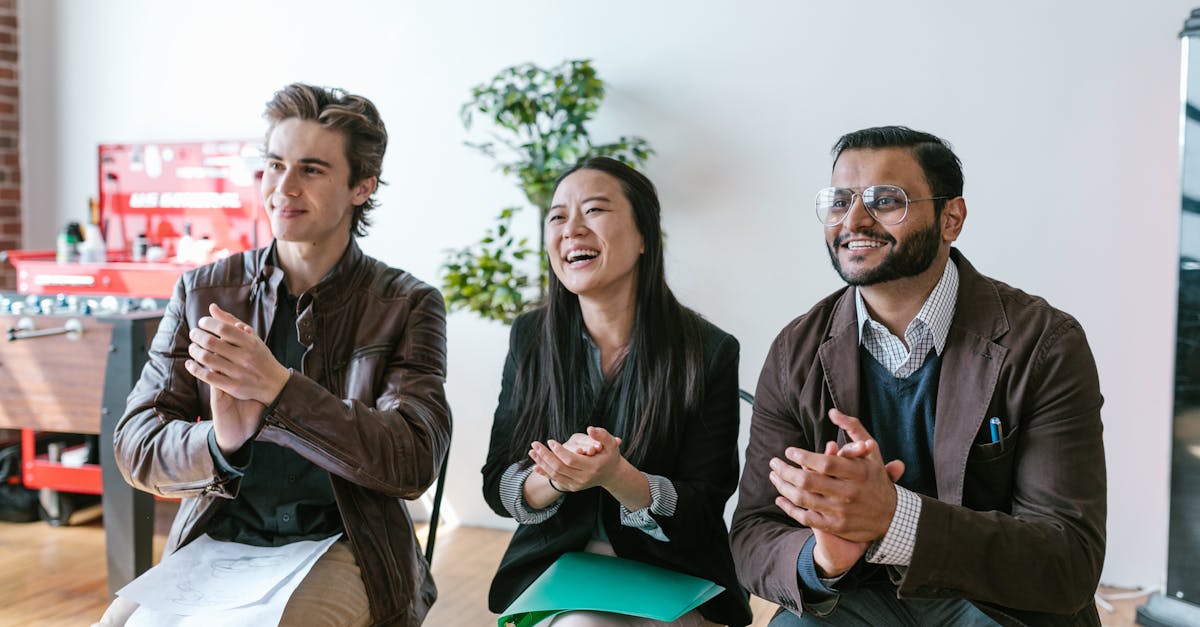 Three diverse team members clapping and smiling during an indoor meeting, showing positivity and teamwork.