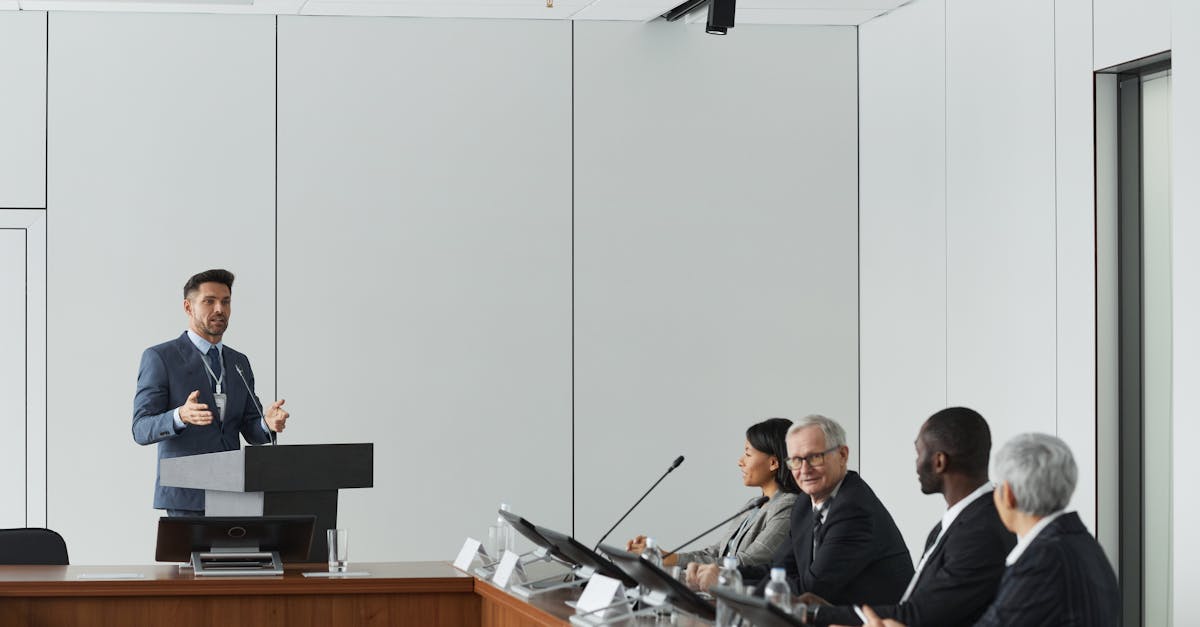 Formal business meeting with a speaker at the podium addressing a diverse panel in a conference room.