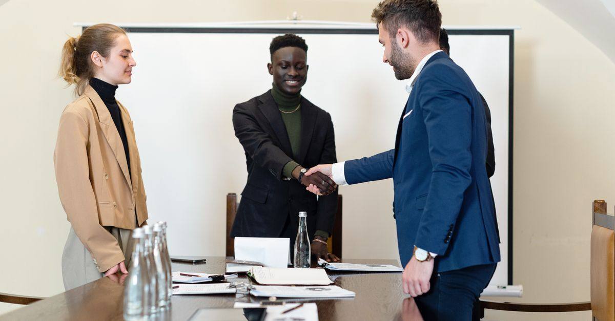 A diverse group of business professionals in a meeting room, shaking hands as a sign of agreement.