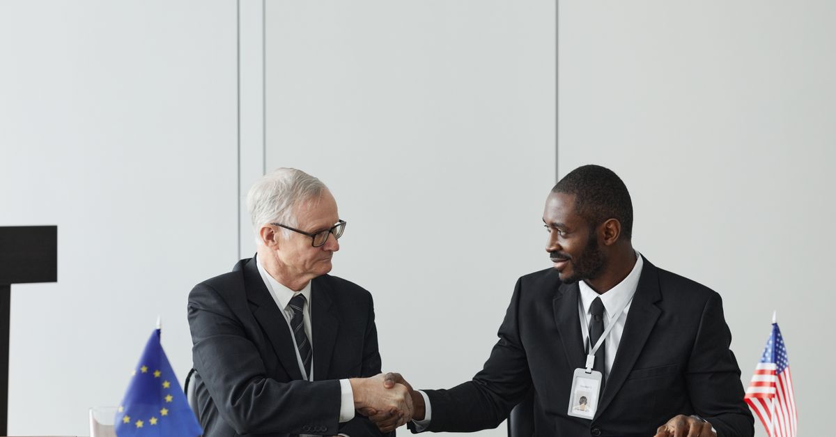 Corporate handshake between diverse businessmen representing EU and US flags, symbolizing partnership and collaboration.