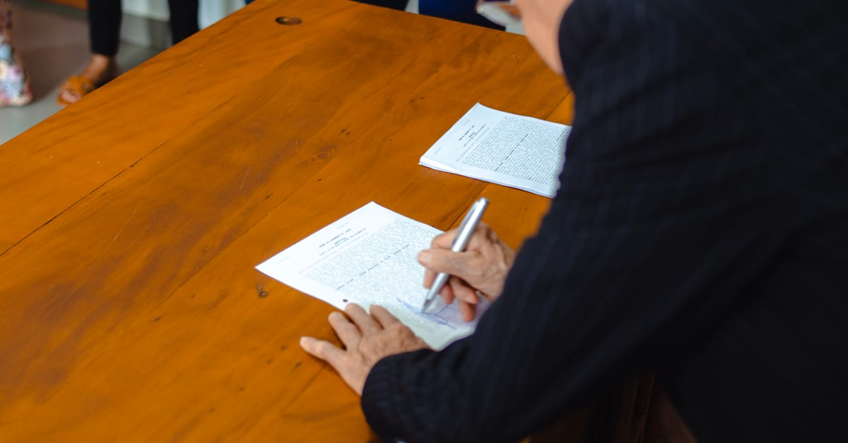 A close-up of a businessman signing official documents at a wooden desk.