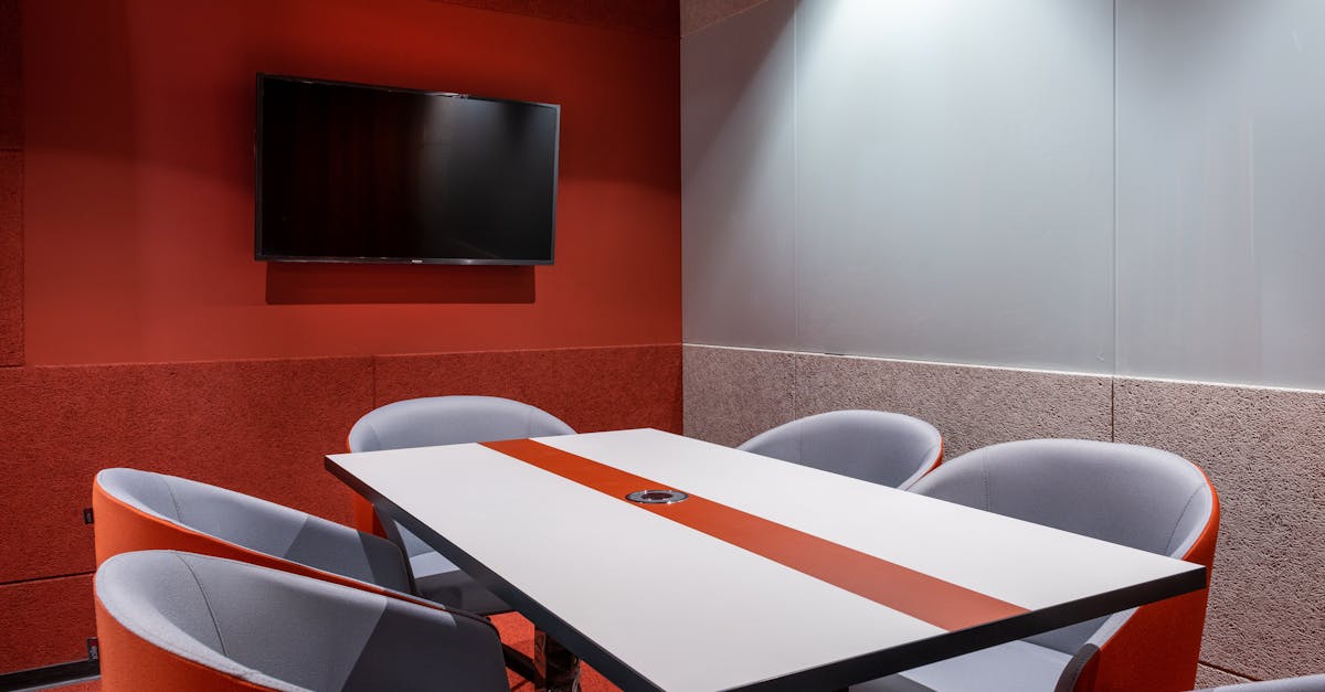 Orange comfortable chairs placed around white table against red wall with TV in stylish office of contemporary financial business center