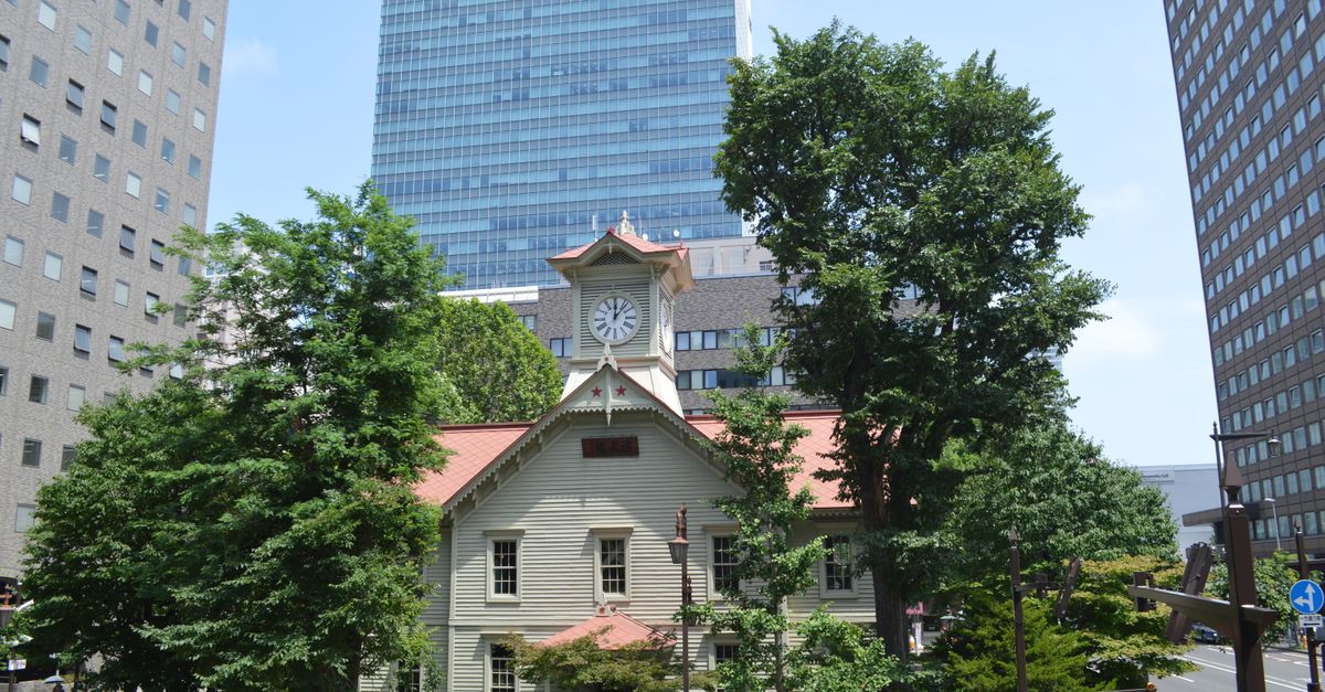 Daytime view of Sapporo's iconic clock tower surrounded by modern buildings and trees.