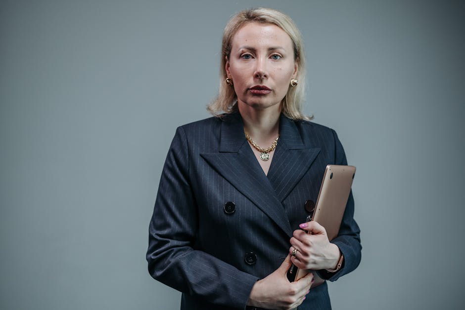 Blonde businesswoman in a black blazer holding a tablet, exuding confidence.