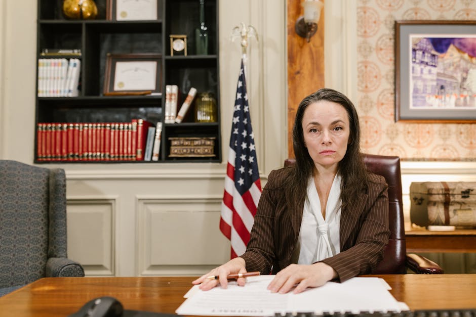 Confident female lawyer at her desk in a law office with legal books and the American flag.