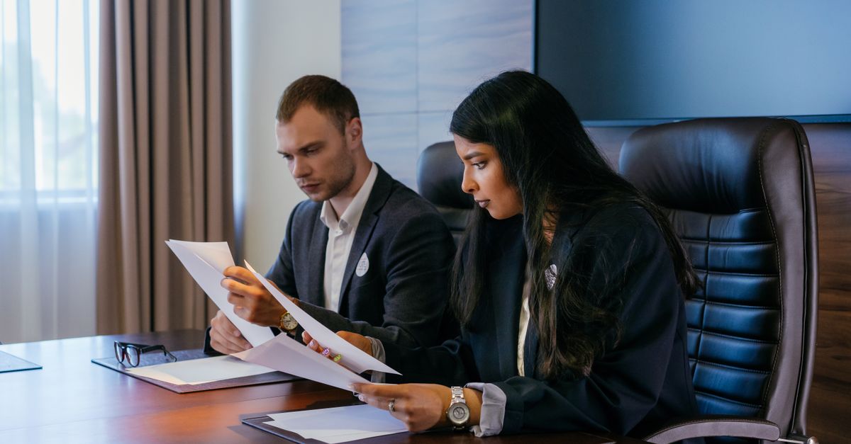 Two business professionals in a conference room engaged in a meeting and document review.