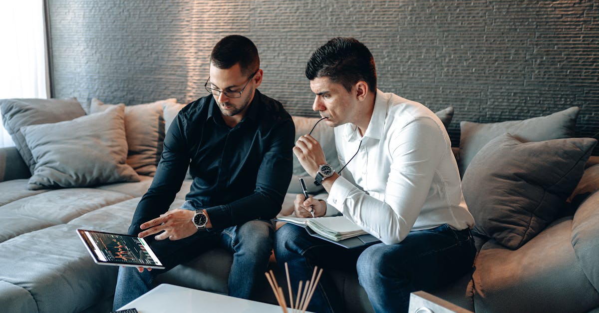 Two business professionals on a sofa analyzing financial graphs on a digital tablet indoors.