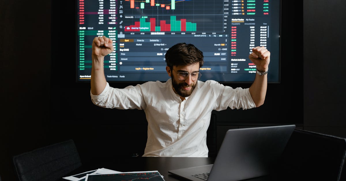 Businessman celebrates stock market success with hands raised in excitement at a trading desk.
