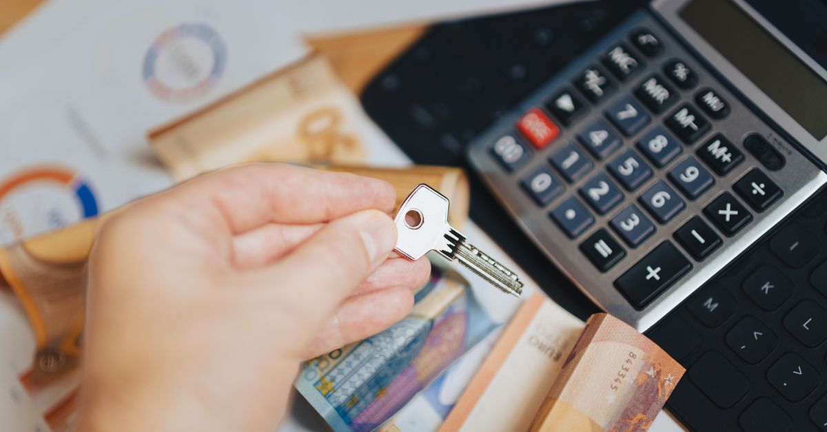 Hand holding key above Euro banknotes and calculator, symbolizing real estate investment.