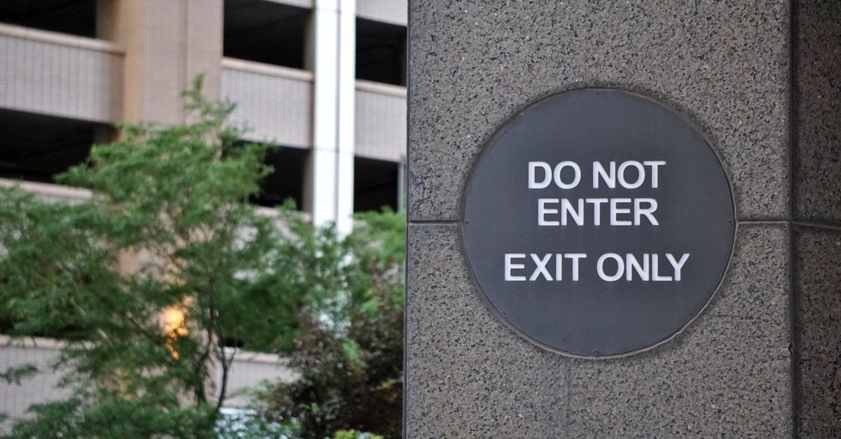 A 'Do Not Enter' sign on a concrete wall outside a building with greenery.