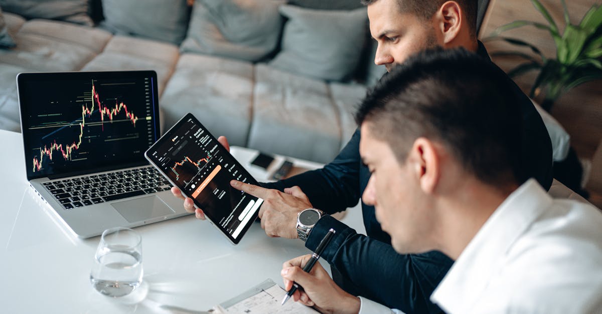 Two businessmen discussing financial charts on devices at a modern indoor setting.