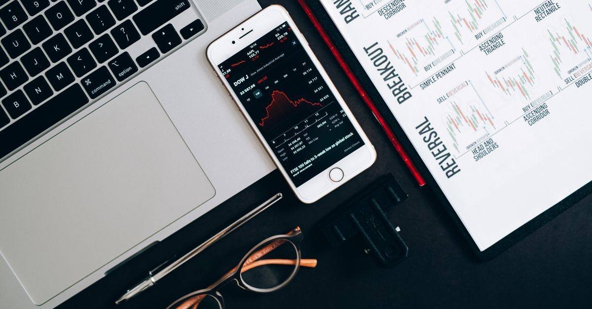 Top view of financial tools including a laptop, smartphone with stock data, and charts for market analysis.