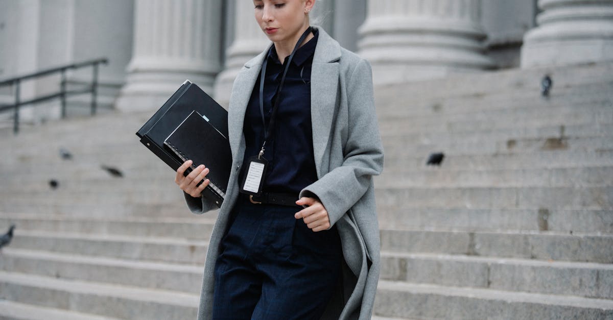 Professional woman in formal attire walking down courthouse steps holding folders outdoors.