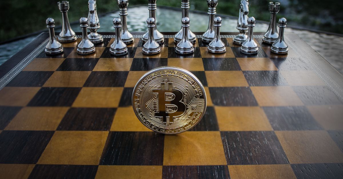Bitcoin coin standing on a chessboard with silver and brass chess pieces. Concept of strategic digital currency investment.