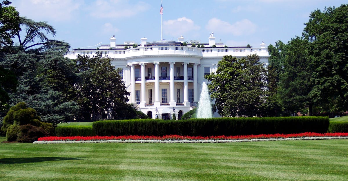 Iconic view of the White House with lush gardens and a central fountain on a sunny day.
