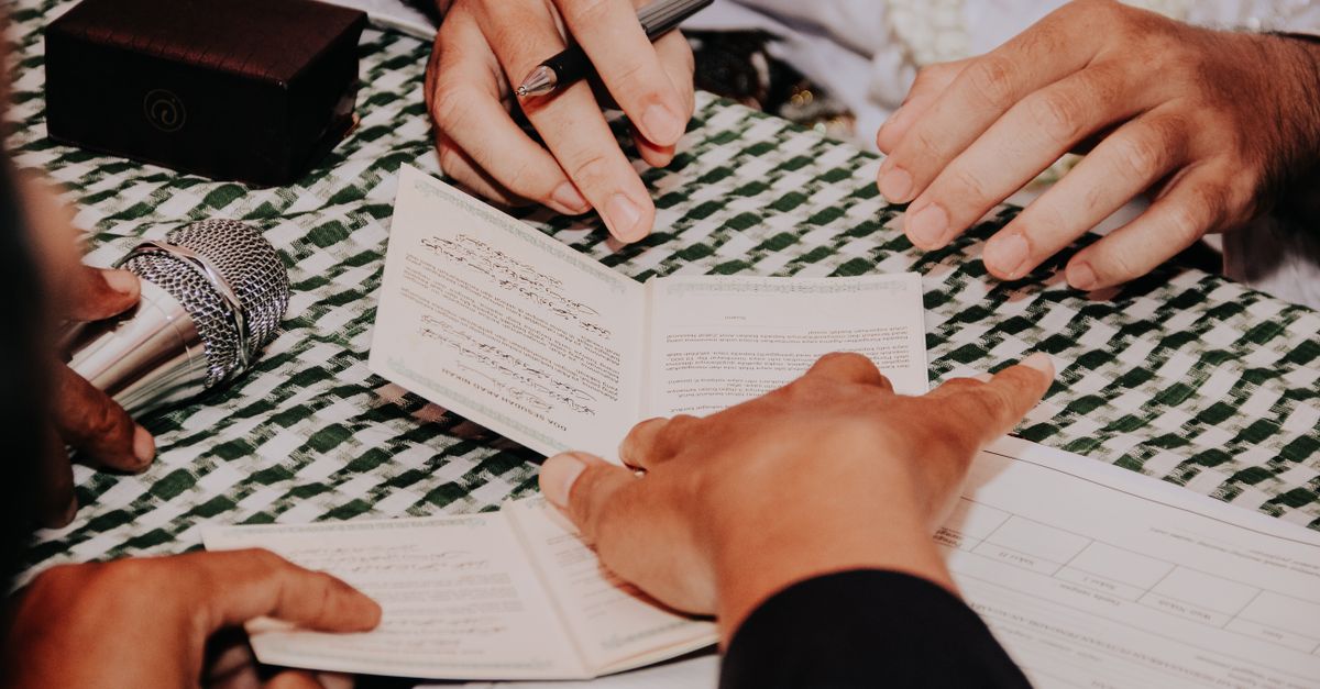 Multiple hands holding and signing a document during a formal ceremony with a microphone nearby.