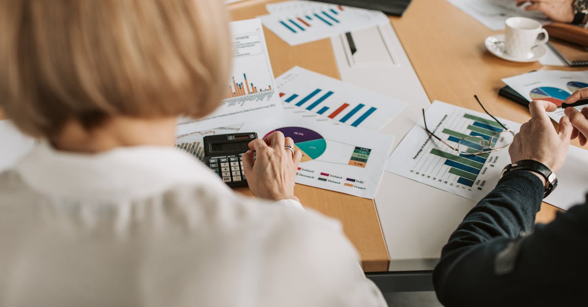 Overhead view of professionals discussing financial graphs and using calculators in an office setting.