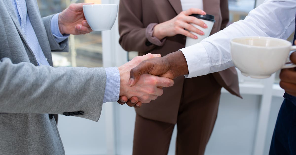 A professional handshake between colleagues holding coffee cups, symbolizing collaboration.