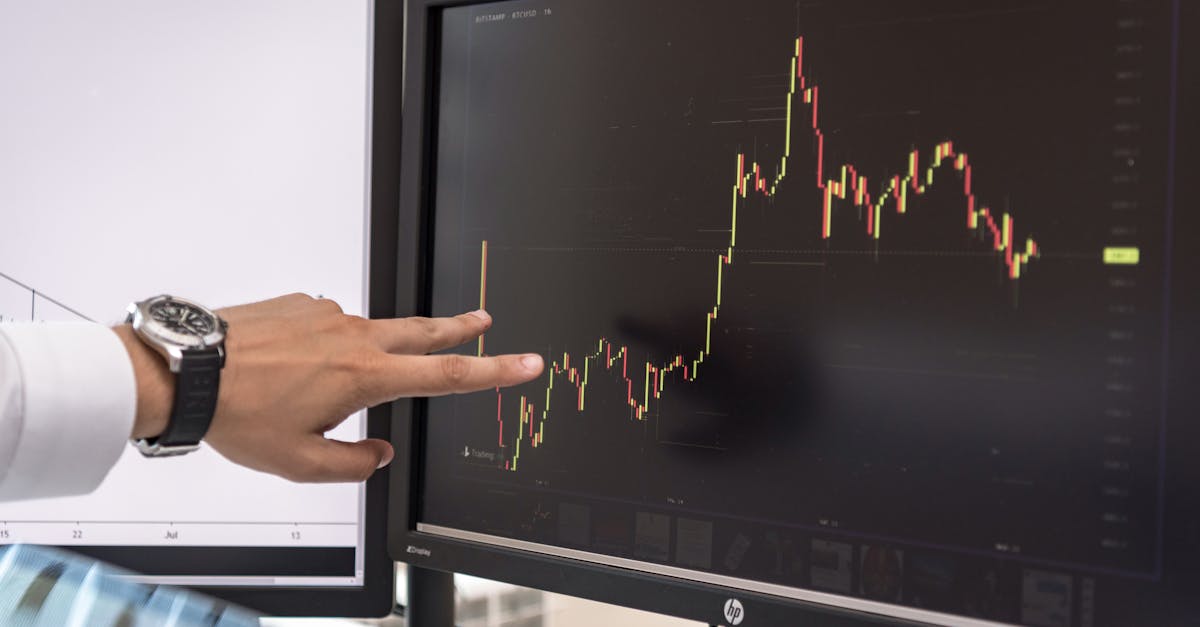 Detailed view of a hand pointing at a cryptocurrency trading graph on a monitor.
