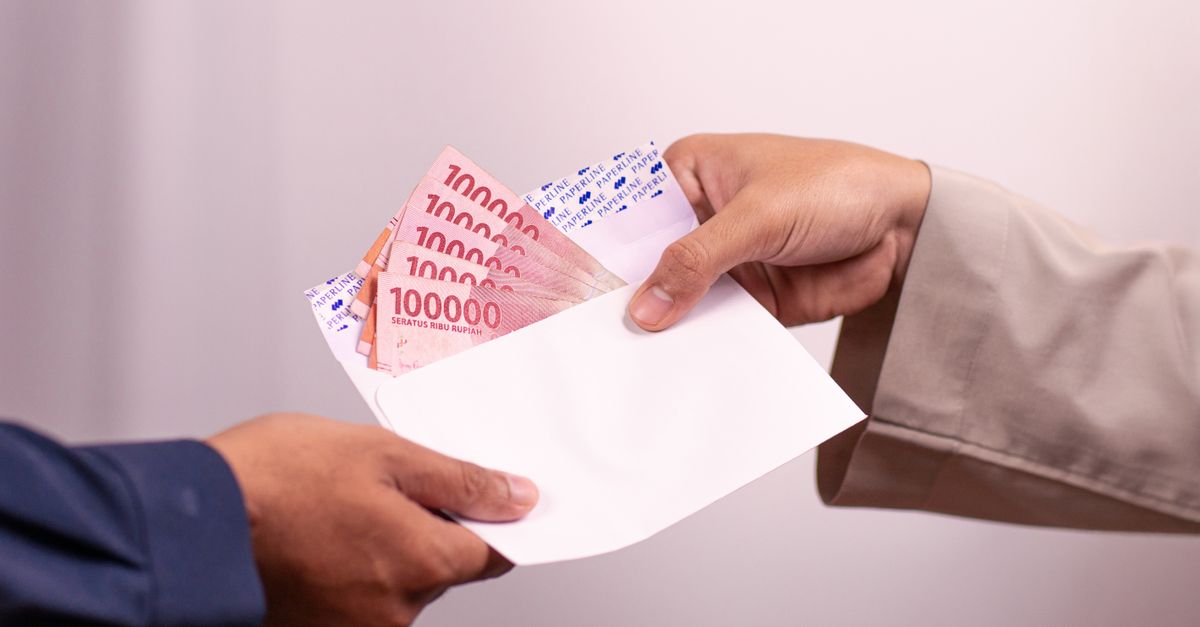 Hands giving and receiving Indonesian rupiah in an envelope, symbolizing financial transaction.