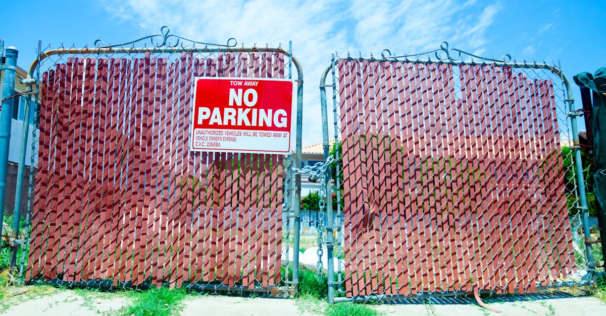 Red 'No Parking' sign on a metal gate with a vibrant blue sky background.