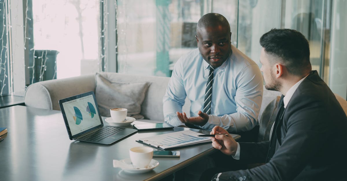Two business professionals engaged in discussion over laptops and documents.