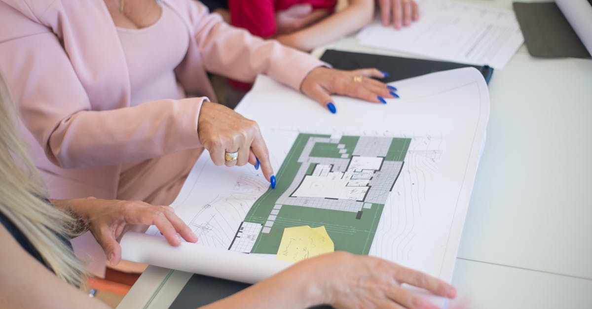 A real estate agent in a pink blazer shows floor plans to clients, discussing property details.
