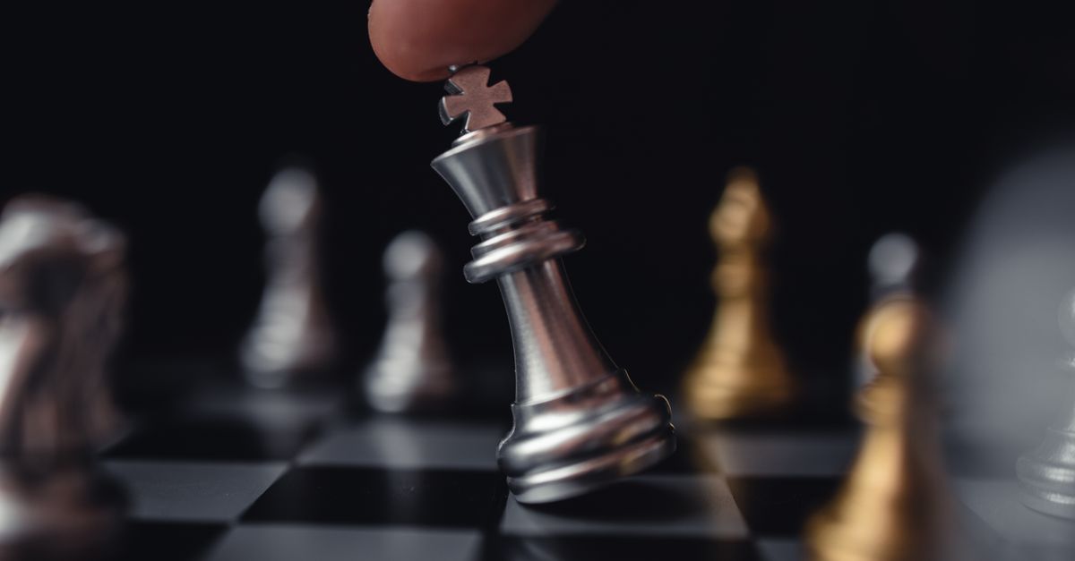 Intense focus on a hand moving a silver king chess piece in strategic play.
