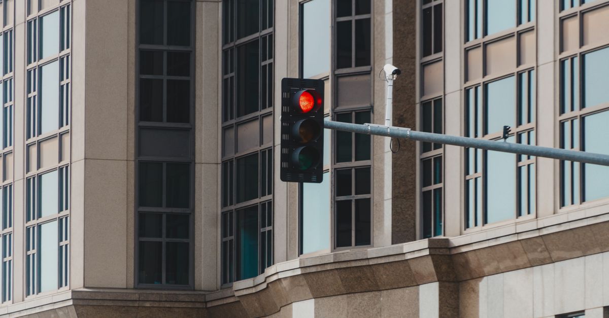 Red traffic light in cityscape setting with modern glass building facade.