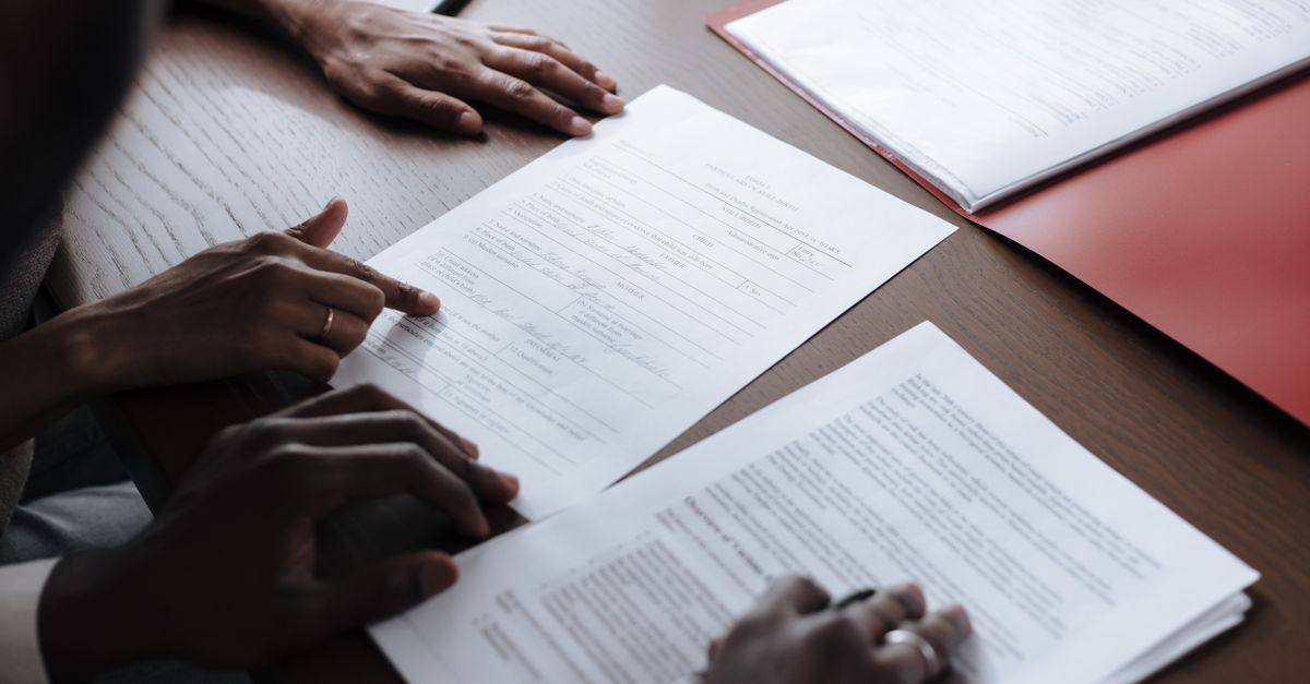 Two individuals reviewing and signing official documents in an indoor setting.
