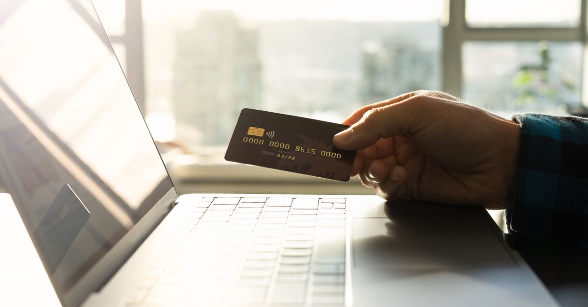 A hand holding a credit card in front of a laptop, symbolizing online shopping and digital payment.