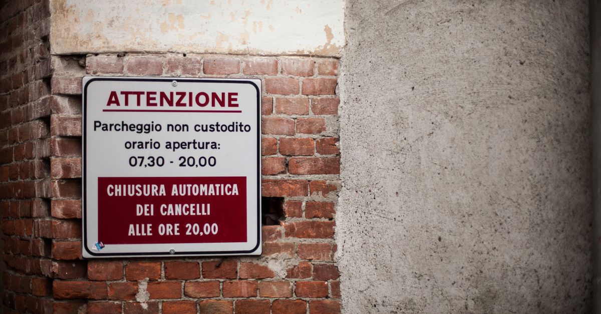 Italian parking warning sign on brick wall. Indicates gate closure times.