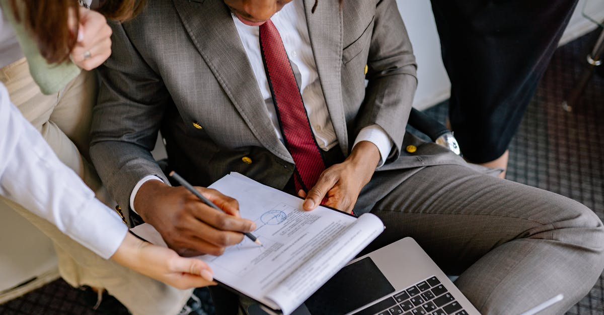 A businessman in a suit signing a contract with colleagues' assistance.