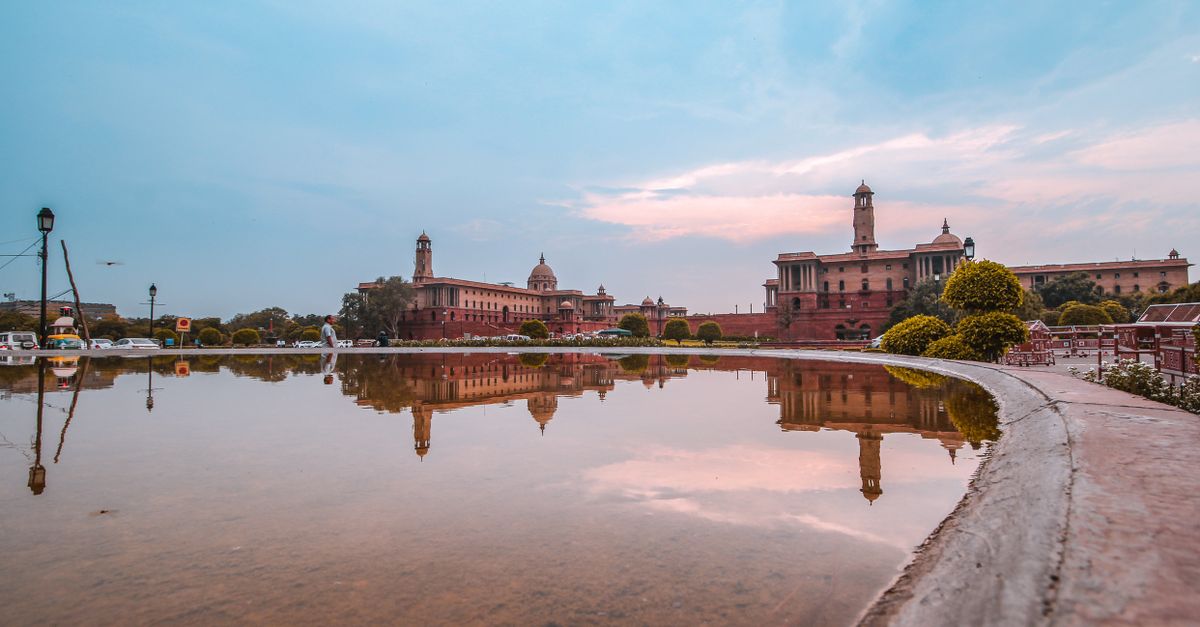 A serene reflection of Rashtrapati Bhavan in a water pond during a vibrant sunset.