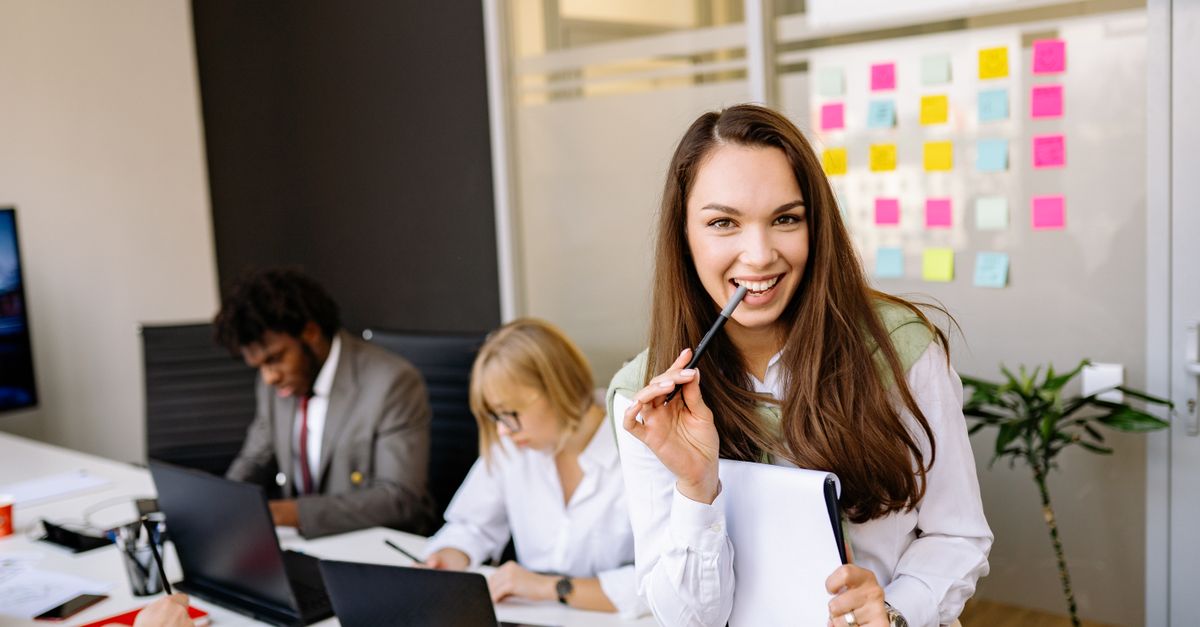 Smiling businesswoman in corporate office with colleagues working in the background.