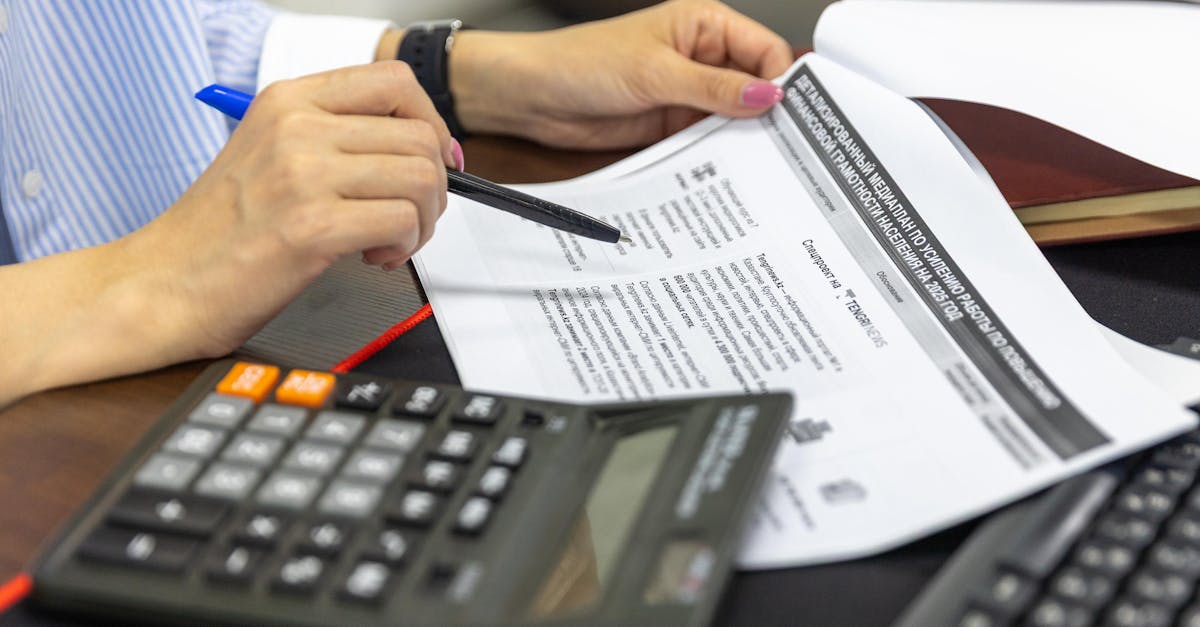 Close-up of a person analyzing financial documents using a calculator and pen.