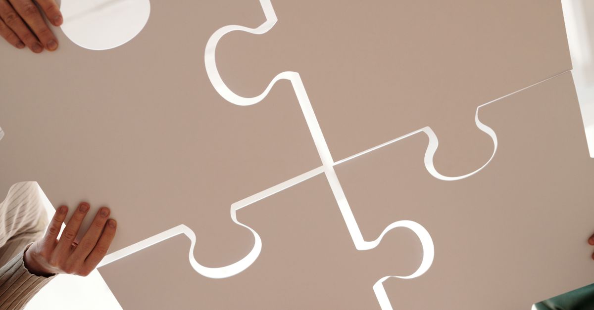 Hands of diverse individuals holding large puzzle pieces, symbolizing teamwork and unity.
